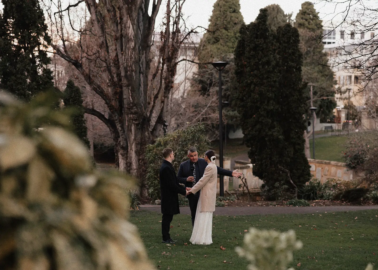 A joyful black and white moment between a couple and their wedding celebrant, Josh Withers, in a park in Hobart, Tasmania. The couple laughs as they exchange vows in an intimate elopement ceremony.